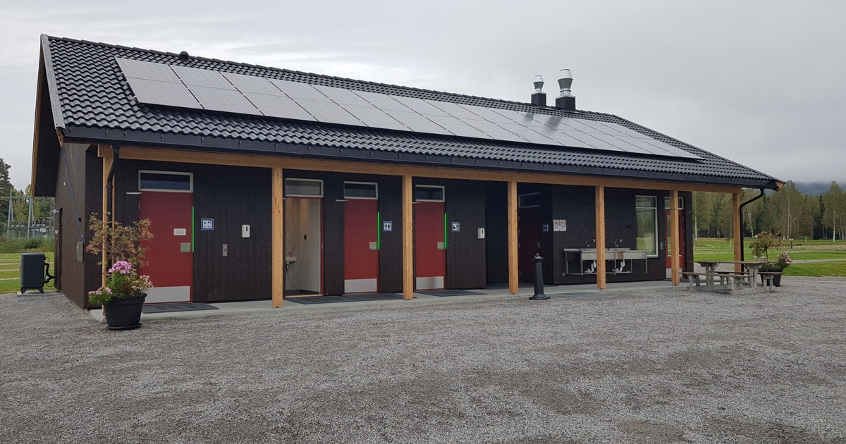 Et brunt bygg med toaletter med solcelle på taket