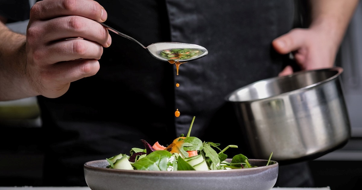 Kokk som danderer tallerken med saus ved hjelp av en skje