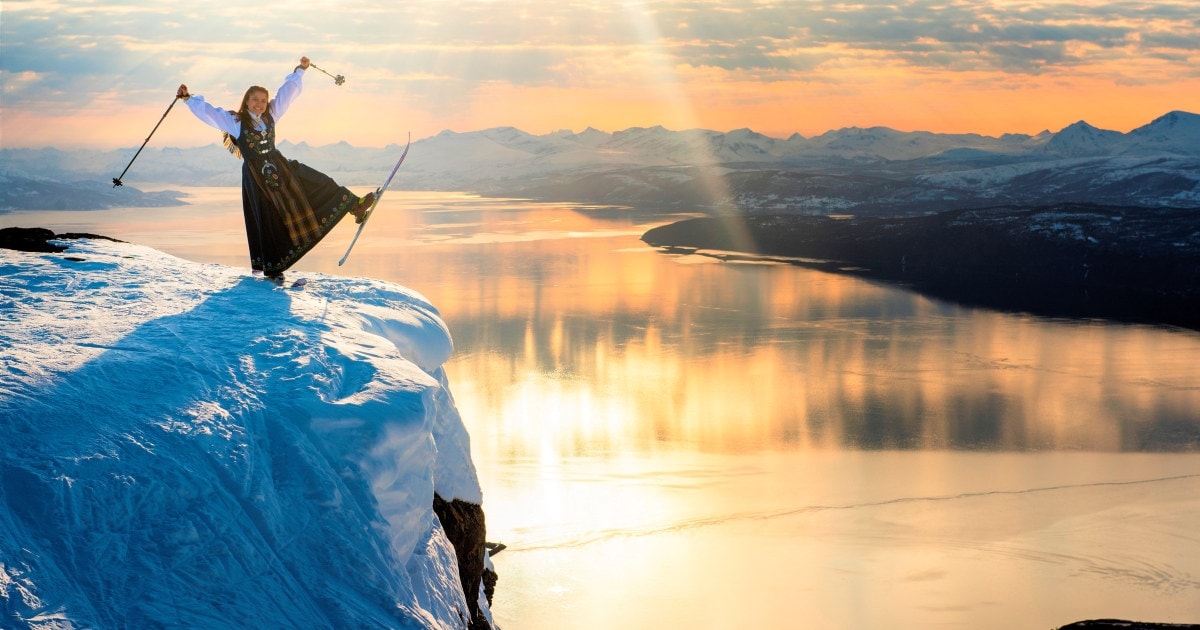 en glad jente på en topp av et fjell som har på seg ski og bunad