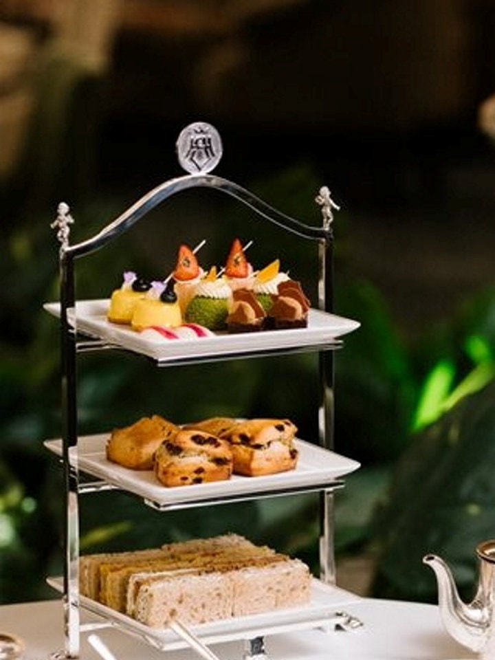 Et bord dekket til afternoon tea med etasjefat med kaker, tekanne i sølv og grønt porselen. Foto