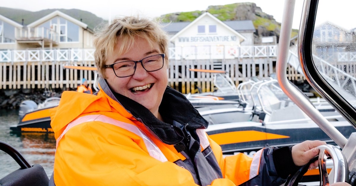 En kvinne med stort smil i  førersetet i en båt. Foto.