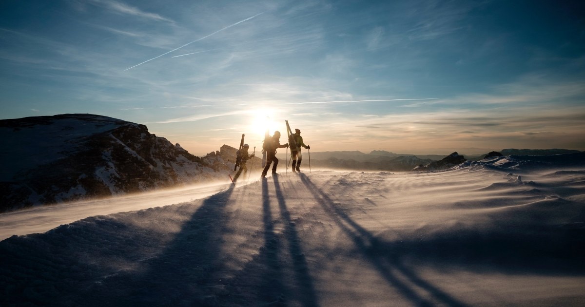 tre mennesker på topptur på et fjell i solnedgangen