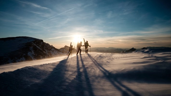 tre mennesker på topptur på et fjell i solnedgangen