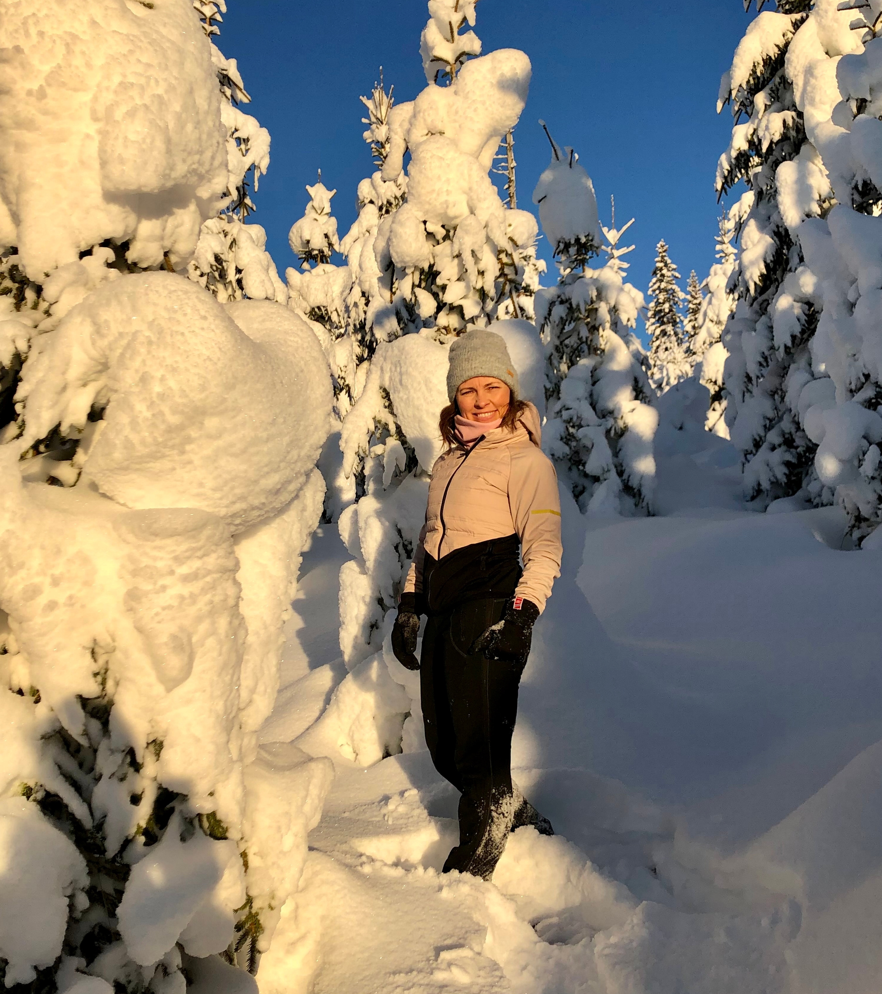 En blid dame som smiler til kamera ute i naturen med masse snø rundt seg og strålende sol.