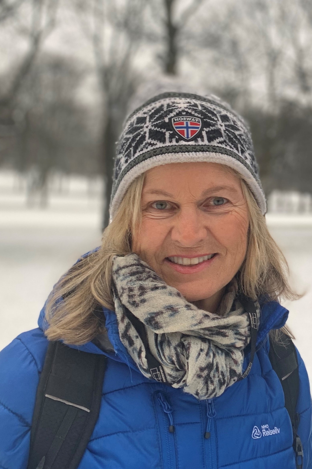 Kvinne med strikkeluelue og blå NHO Reiseliv-jakke i vinterlandskap