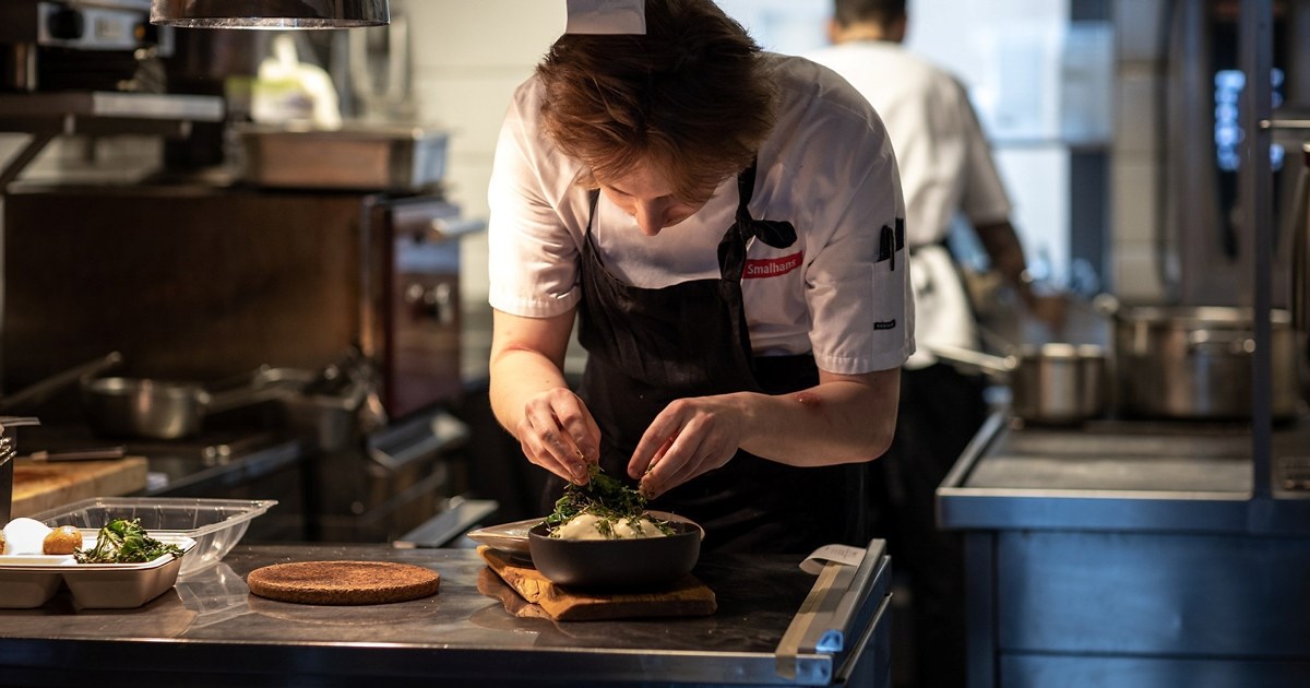 Ung kokk som legger garnityr på en tallerken, på et restaurantkjøkken. Foto.