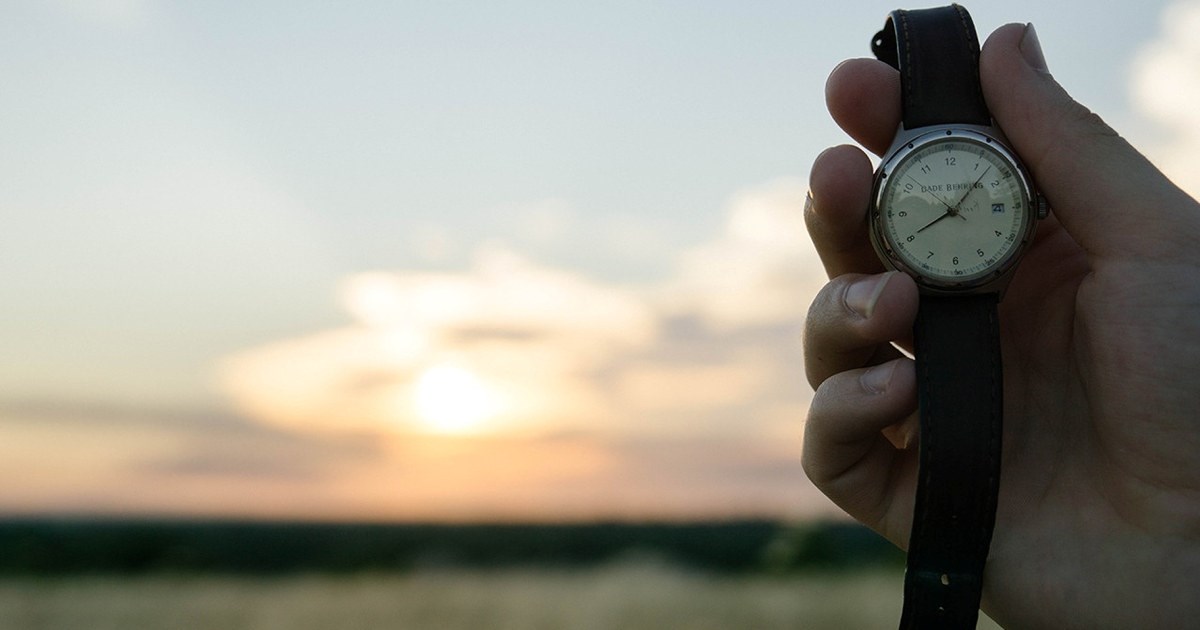 Foto av en hånd som holder opp et armbåndsur. En lys himmel sees i bakgrunnen.