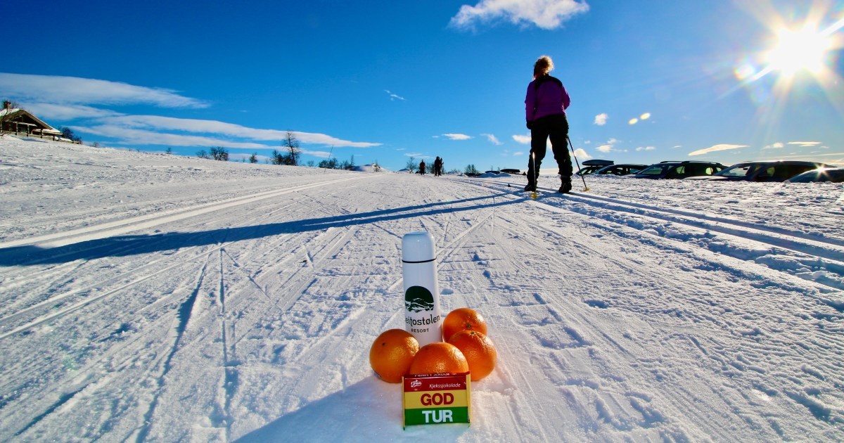 Naturbilde med en skiturist og kvikklunsj, termos og klemmentinger som står i snøen.