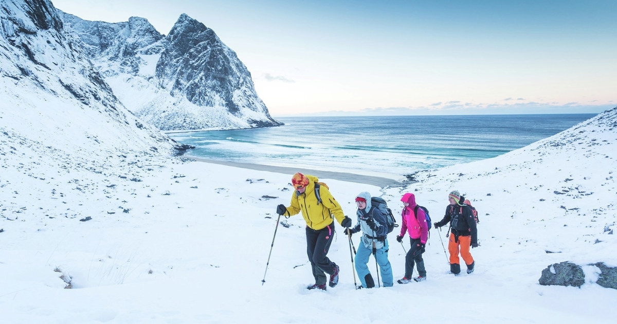 Mennesker som går på ski på et snødekket fjell ved vannet. Foto.