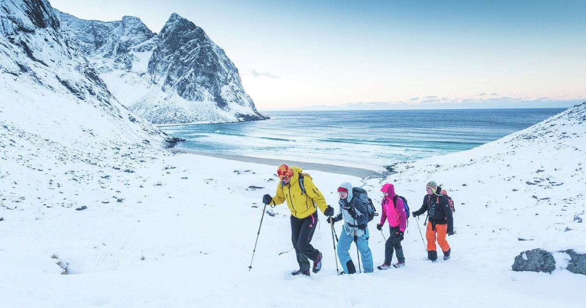 Mennesker som går på ski på et snødekket fjell ved vannet. Foto.