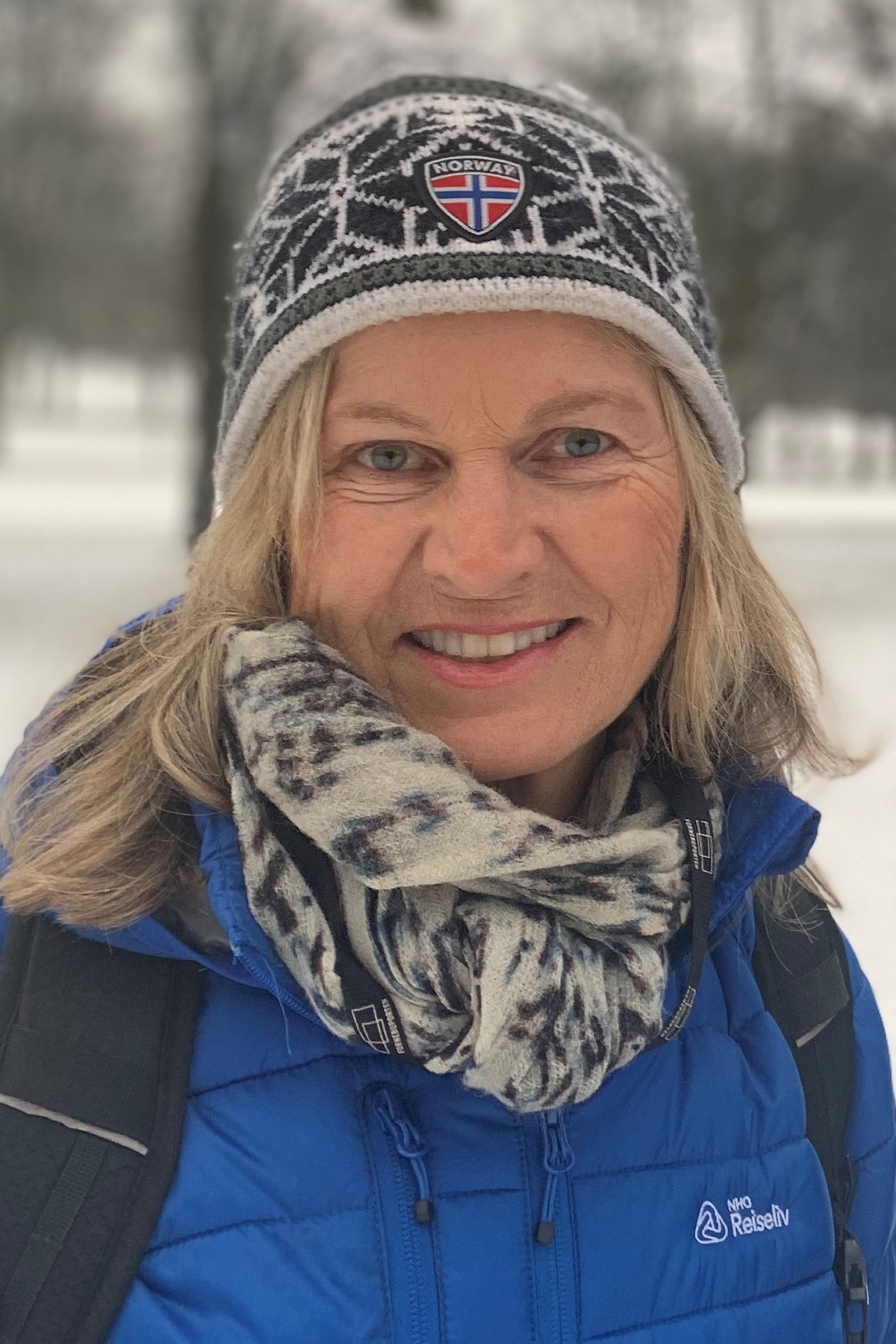 Kvinne med strikkeluelue og blå NHO Reiseliv-jakke i vinterlandskap