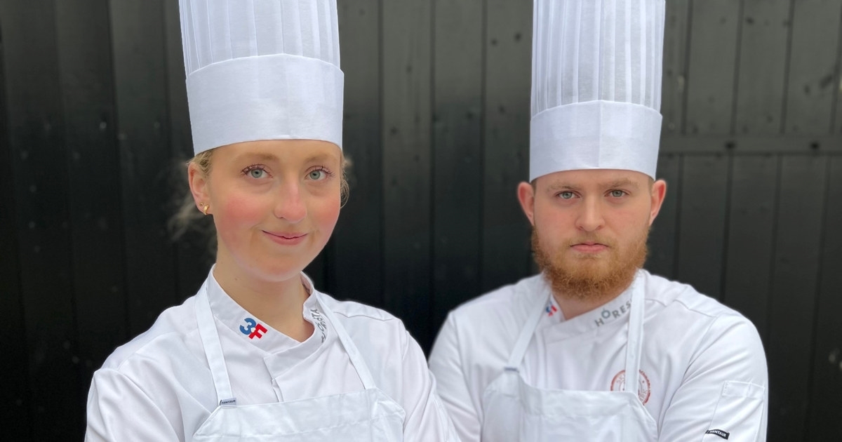 En ung kvinne og en ung mann i kokkeklær og armene i kryss. Foto