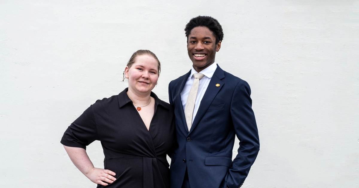 A young woman and a young man, both wearing waiter uniforms. Photo