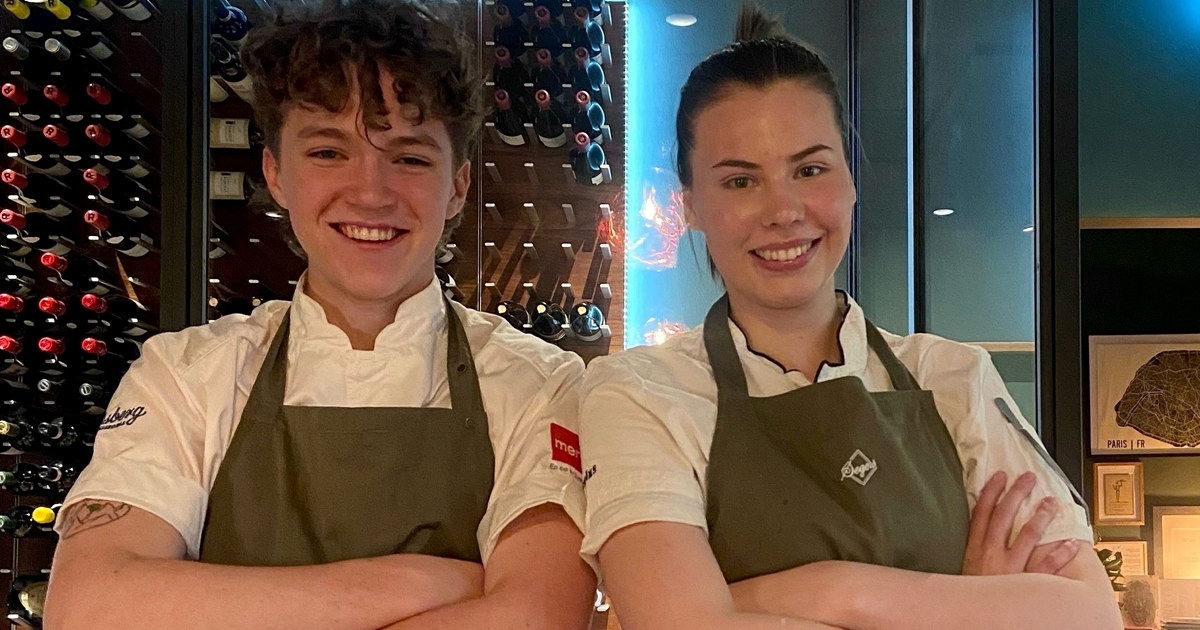 A young man and a young weoman wearing chef jackest and aprons. Photo.