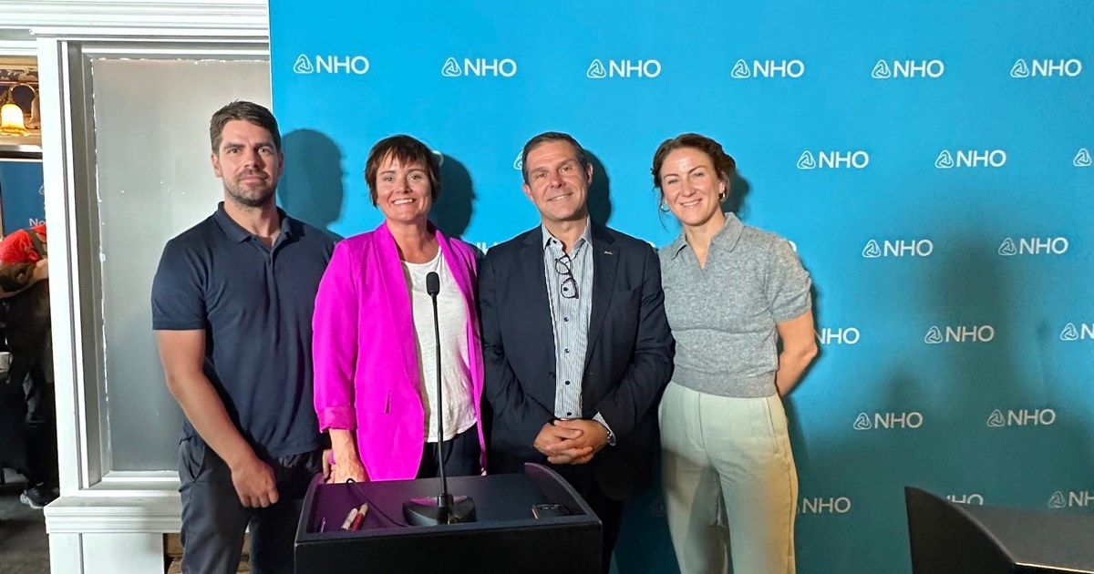 4 personer som står foran en blå NHO pressevegg og smiler til kamera