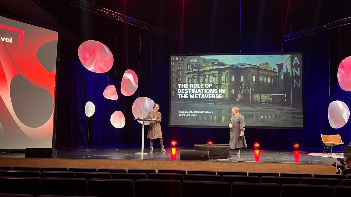 to kvinner som står på en scene foran en presentasjon med teksten "destinasjonenes rolle i metaverset". Foto