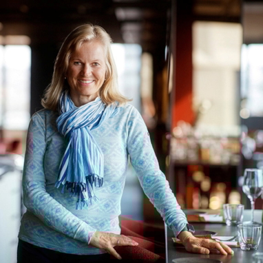 Smilende kvinne som står ved et restaurantbord. Foto