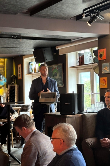 En mann som står på en scene med publikum foran seg. Foto