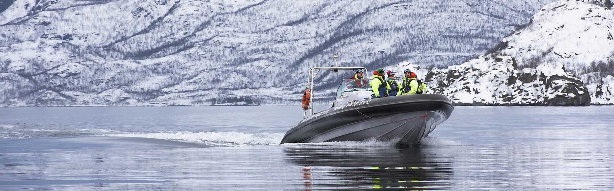 Mennesker i en båt med snødekkede fjell i bakgrunnen. Foto.