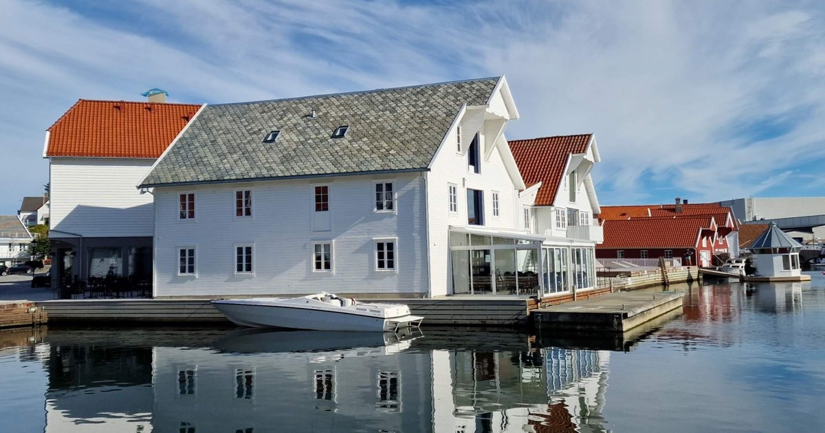 Et hvitmalt hus med brygge ved vannet. En båt ligger fortøyd utenfor. Foto