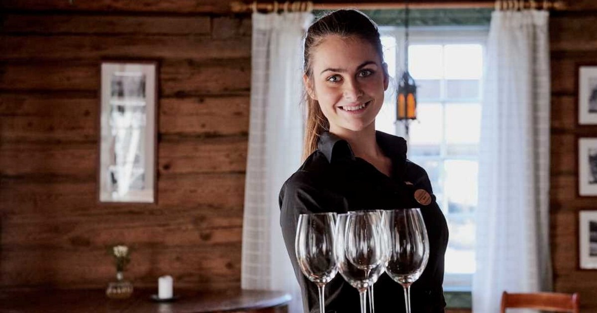 En smilende servitør som står i en restaurant og holder et brett med blankpolerte glass: Foto