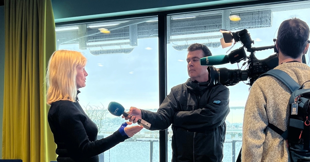 En kvinne som intervjues av to journalister, med mikrofon og kamera. Foto