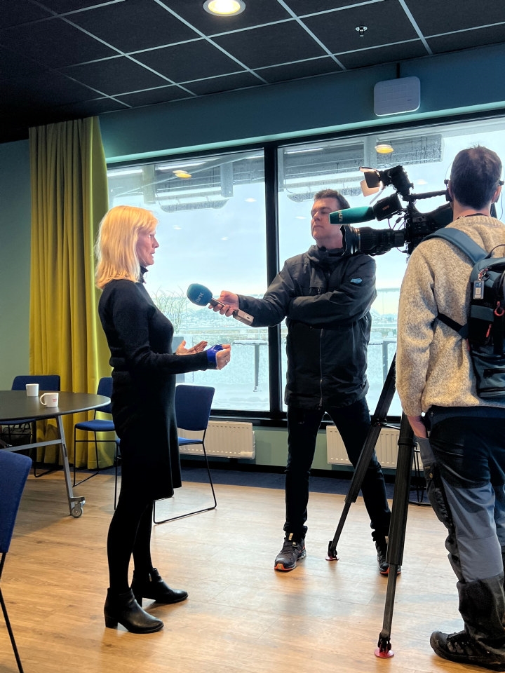 En kvinne som intervjues av to journalister, med mikrofon og kamera. Foto