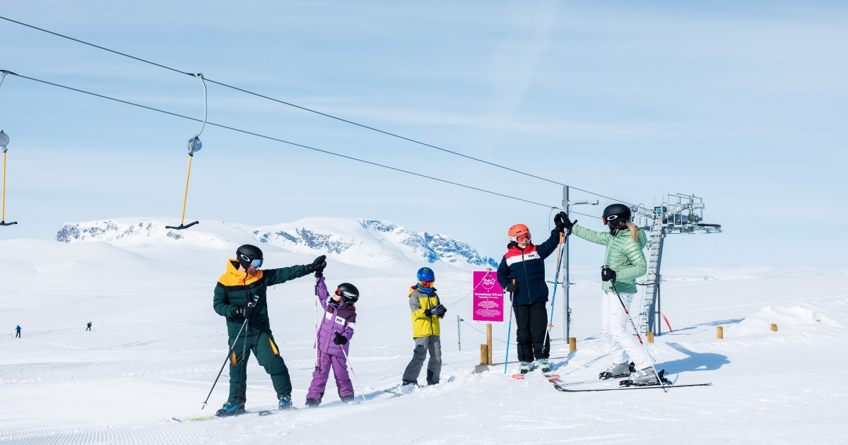 Fem mennesker med alpin utstyr i snødekket landskap med skiheis i bakgrunnen