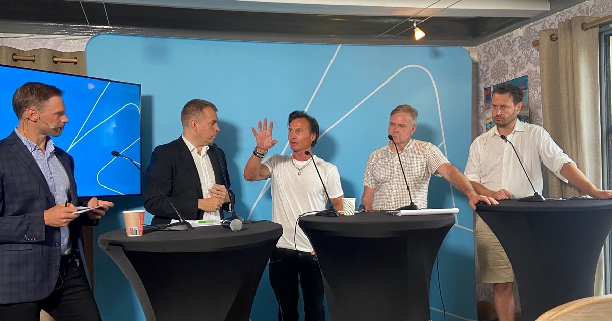 Fem menn som står ved talerstoler med NHO-logoen i bakgrunnen. Den ene mannen holder en hånd opp. Foto.